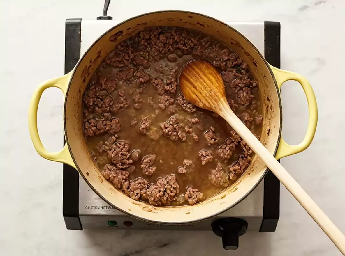 Préparation de la recette chili con carne : le bœuf haché et les bouillons cubes cuisent dans une cocotte jaune, première étape .