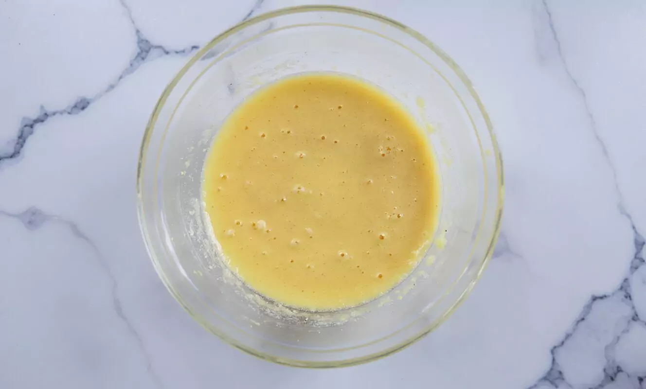 Œufs battus dans un bol en verre pour la recette de frangipane, montrant un liquide jaune doré lisse avec de petites bulles