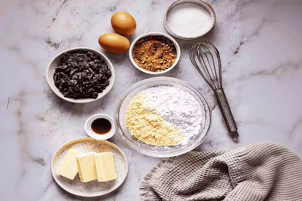 Ingrédients pour cookies sans gluten disposés sur plan de travail : farines de riz et maïs, fécule, chocolat concassé, œufs, beurre et sucres