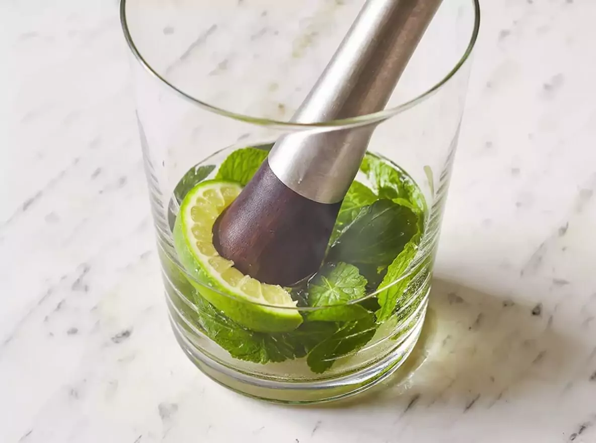 Étape 1 mojito : menthe fraîche et quartier de citron vert écrasés délicatement dans le verre