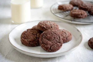 Cookies tout chocolat moelleux disposés sur une assiette blanche avec un verre de lait